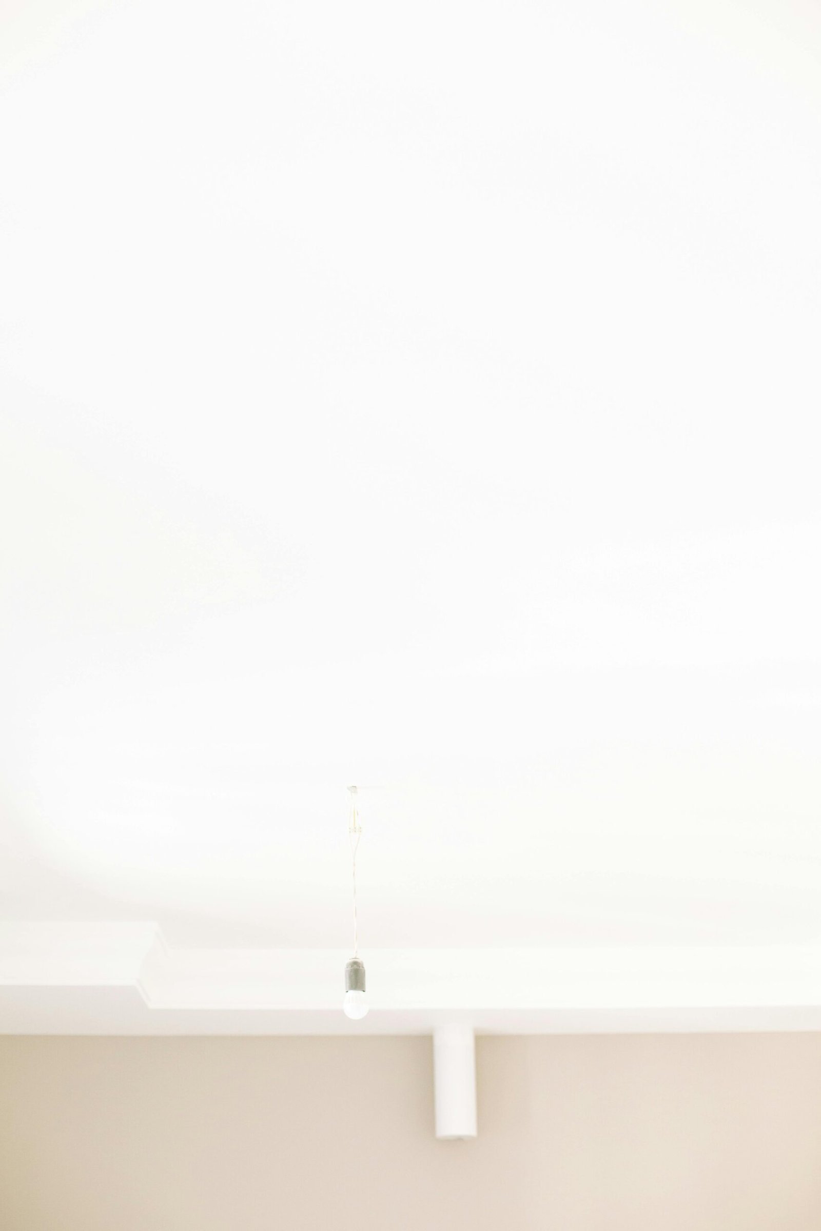 Simple minimalist ceiling design with a hanging light bulb, creating a serene atmosphere.